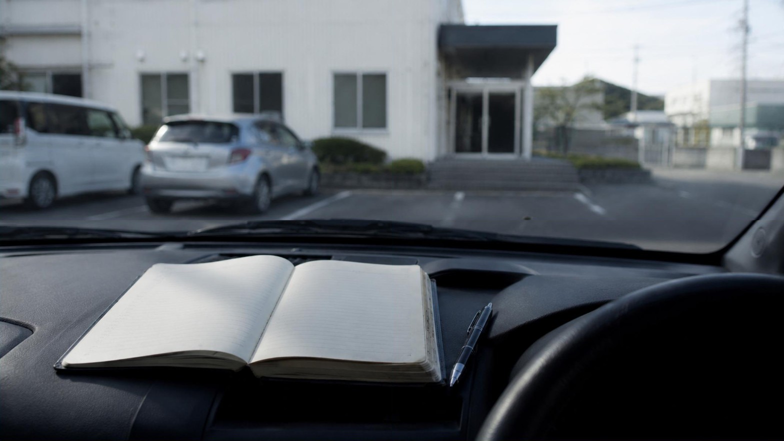 訪問先の駐車場に停めた車の運転席で、手帳を開いて次の行き先を確かめている